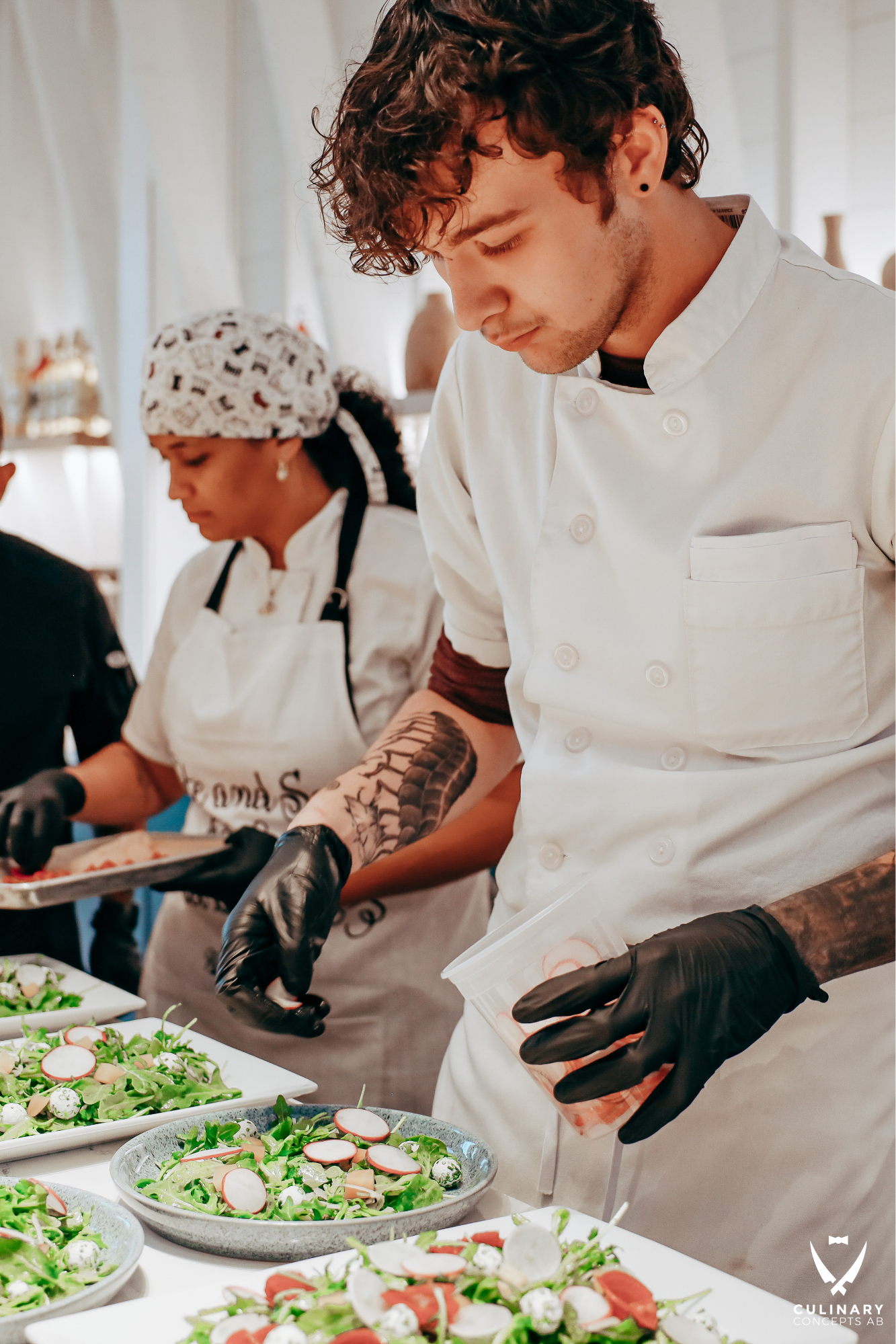 Chef whisking batter in a bowl while students chop ingredients in a bustling kitchen classroom.