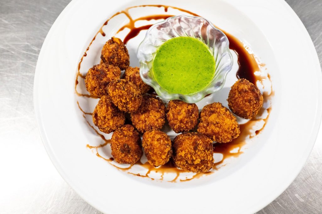 Plated fried croquettes with green herb dipping sauce and drizzled sauce garnish