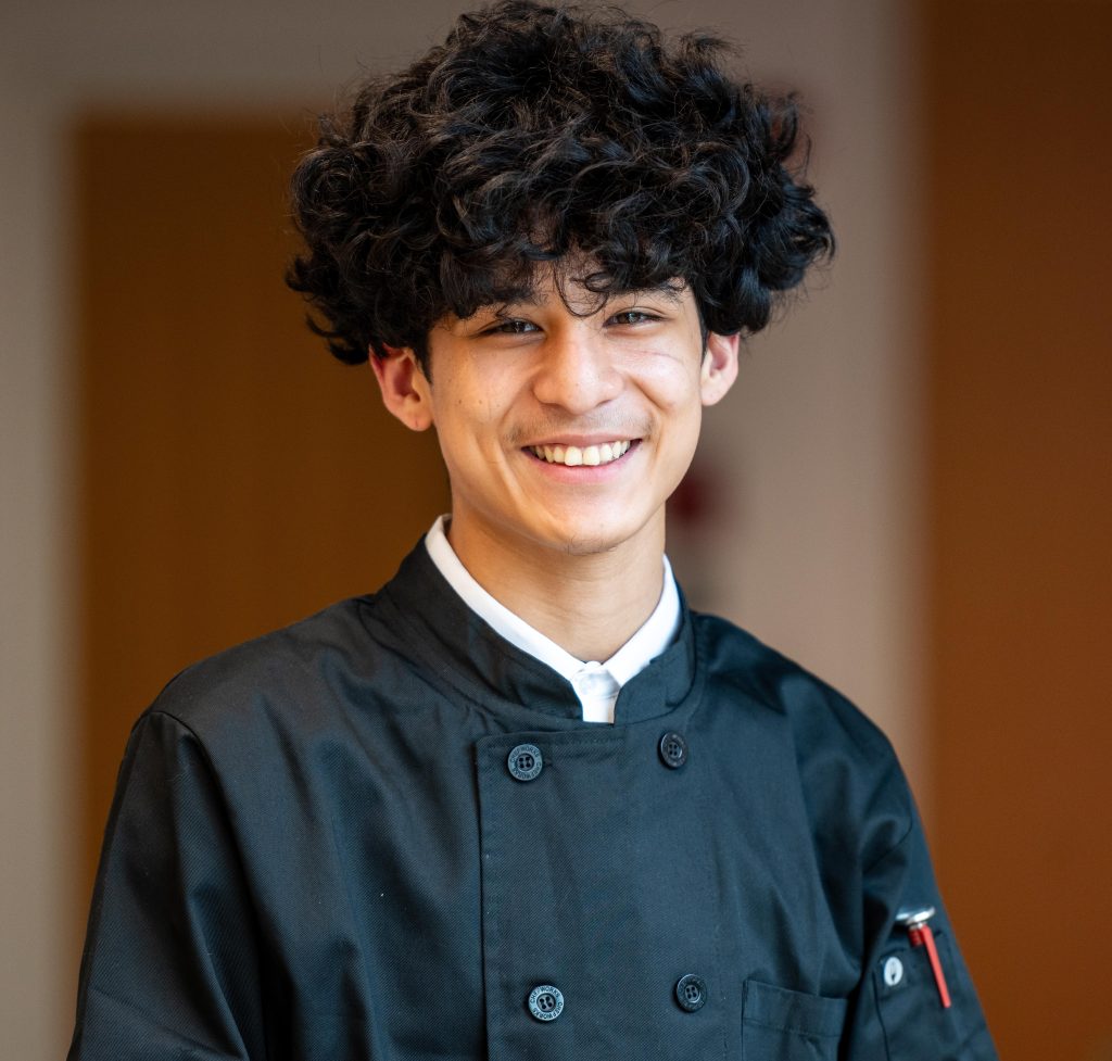 Smiling young chef in culinary career training through the GO Cook program, wearing a chef coat